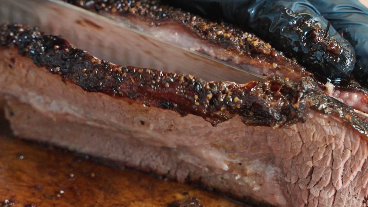 Brisket being sliced, showing a peppery bark