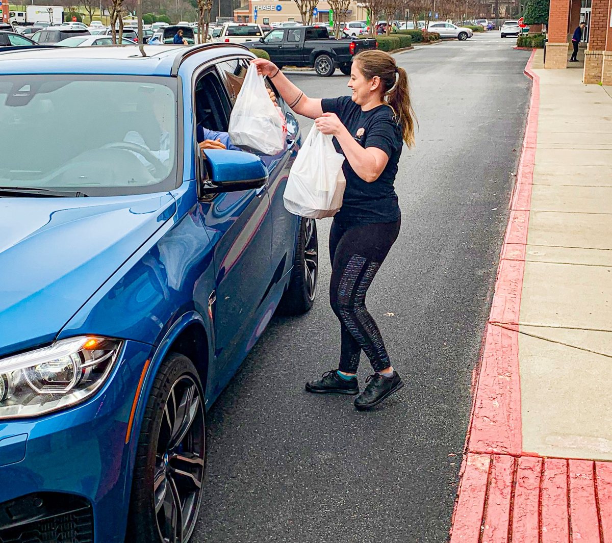 A Righteous 'Que team member handing bagged orders to a customer at curbside pickup