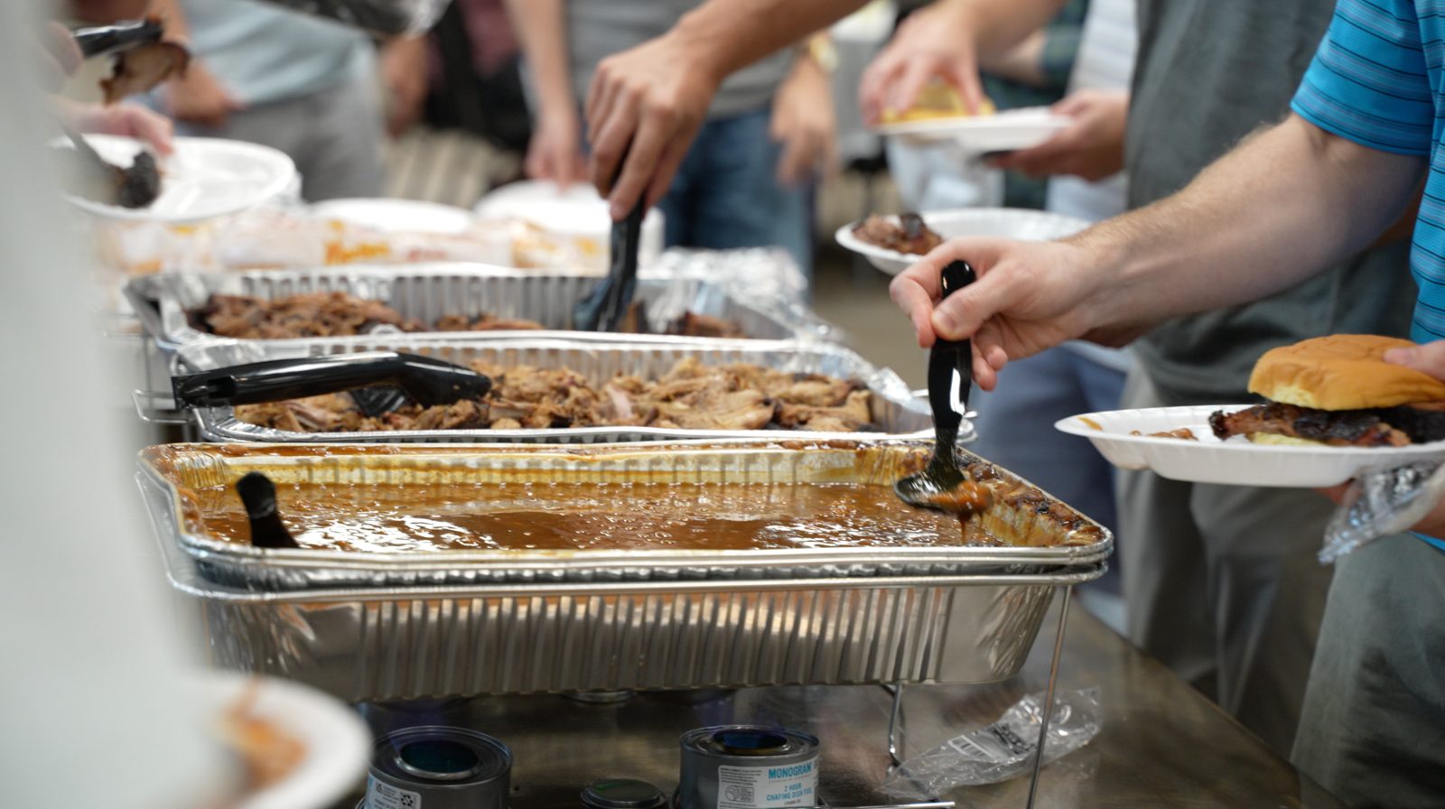 Guests moving down a buffet line of brisket, pulled pork and baked beans