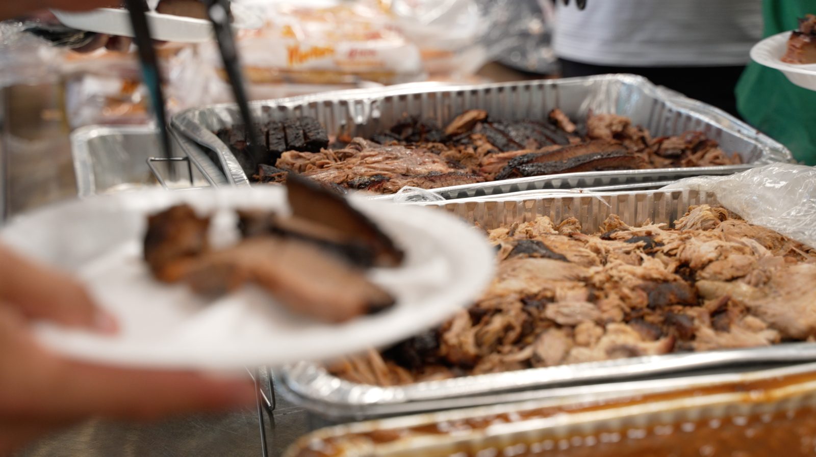 Trays of sliced brisket and pulled pork on a catering line