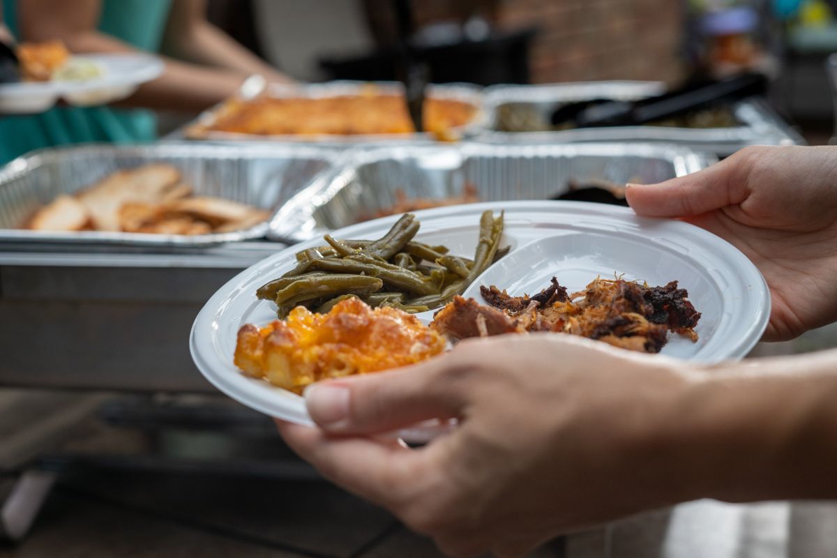 A guest holding a plate of mac and cheese, green beans and pulled pork