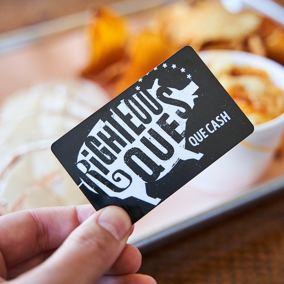 A hand holding a black Righteous 'Que Que Cash gift card