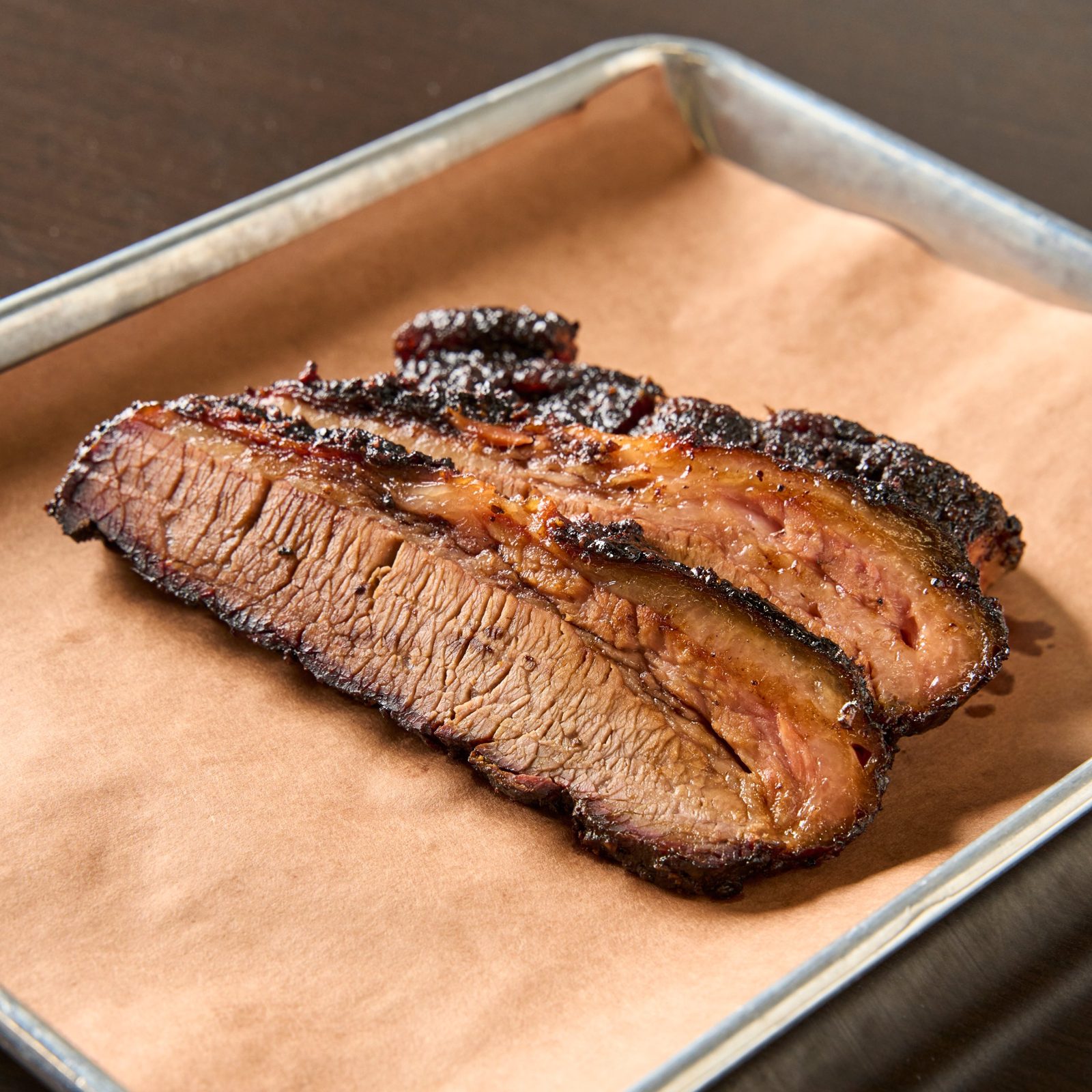 Slices of oak and cherry smoked brisket with a dark peppery bark on butcher paper