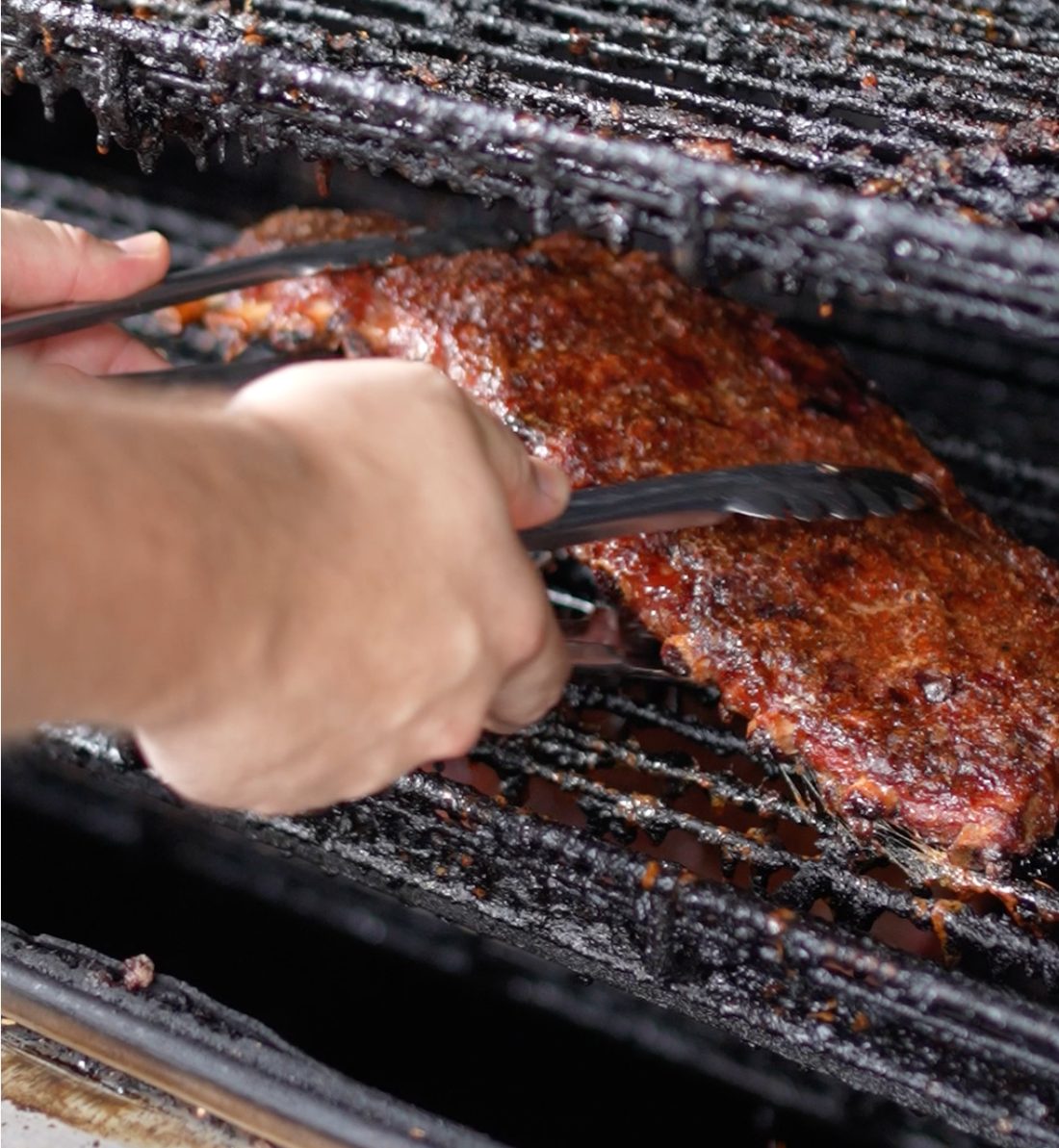 A slab of ribs being pulled off the smoker with tongs